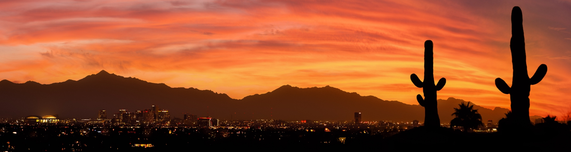 
		Sunset over mountains with Phoenix in foreground and two saguaro cacti.		