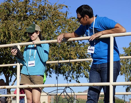 Two research undergraduates taking a reading off an instrument while they are standing by railing.