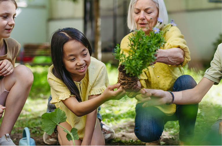 Children with their teacher planting some flowers from a pot