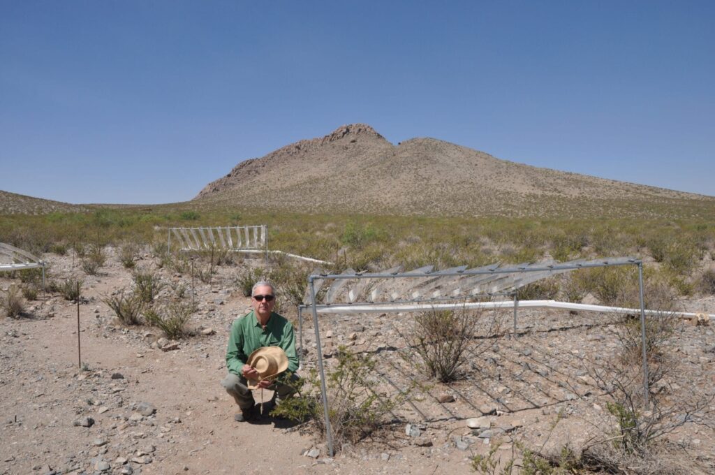 Osvaldo Sala kneeling next to research apparatus in the desert.