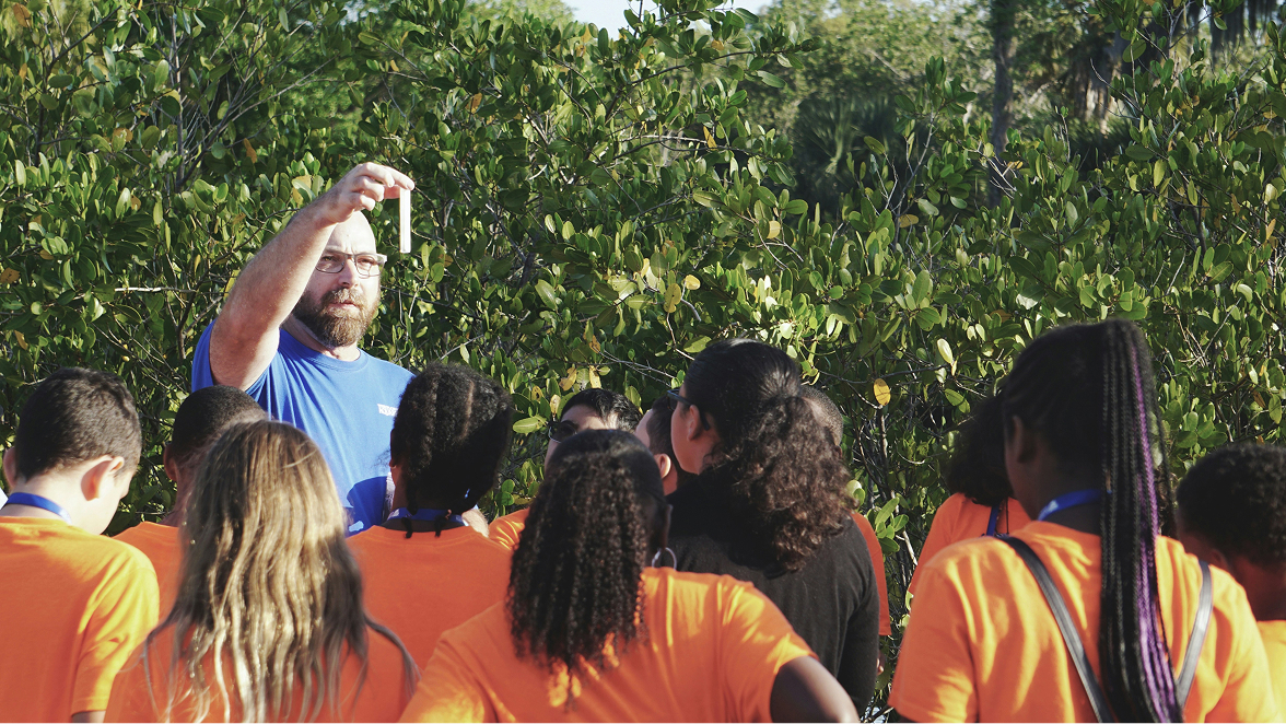 Teacher showing students a testtube while standing outside by trees.
