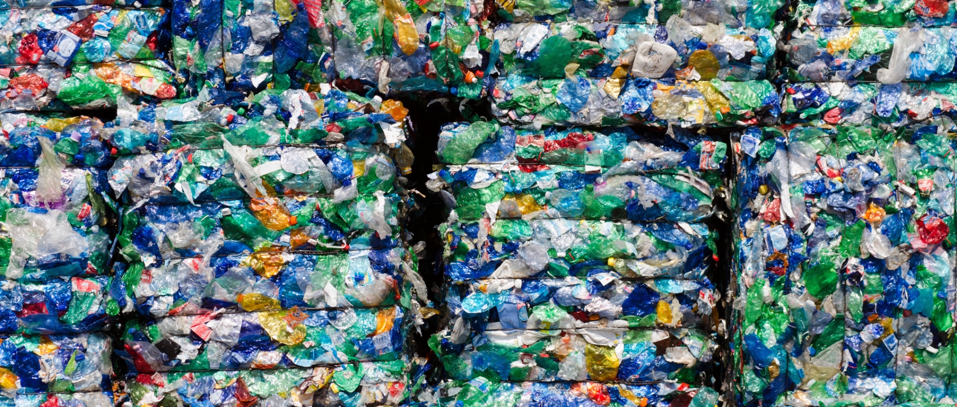 An angled photo showing a wall of compressed plastic bottles in varying shades of blue, green and clear/white with colorful lids.