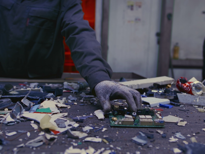 Person reaching for circuit board that is among trash.