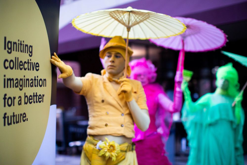 Performers with parasols and a banner that says, "Igniting collective imagination for a better future."