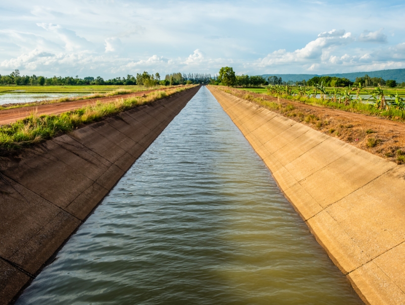 A canal with sloped concrete sides and greenery along the shores.