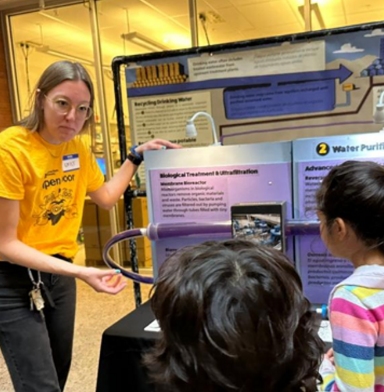 A volunteer explains a nearby research poster to a group of children.