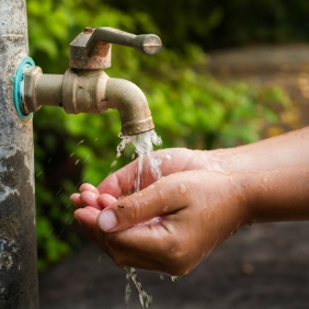 Close-up of someone washing their hands underneath a water spigot.