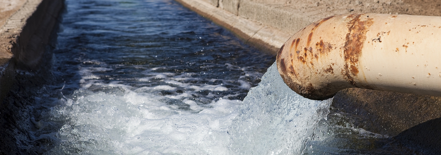 Water flowing from a tan pipe into a manmade canal.